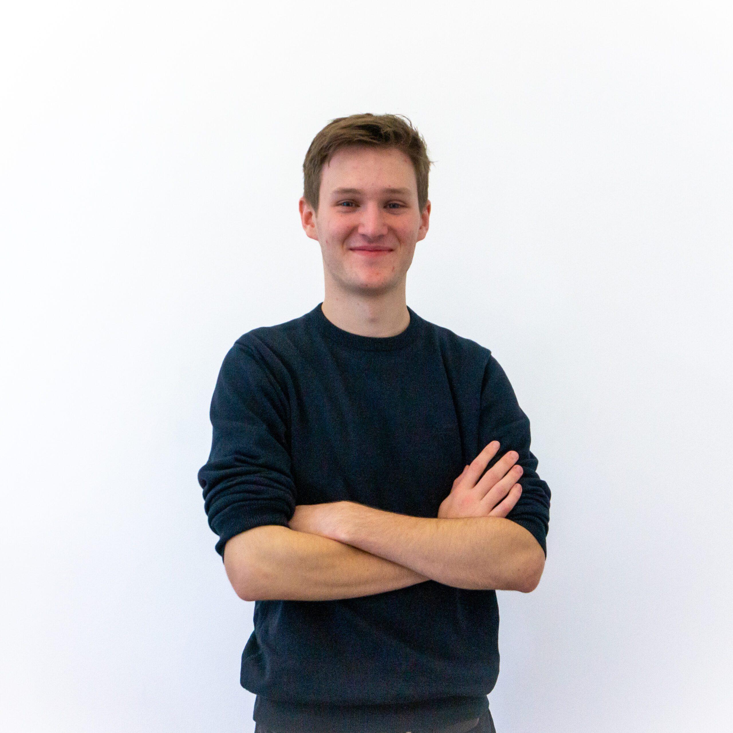 Henry in a dark jumper on standing in front of a white background with his hands crossed ready to get down to some AI lead generation.